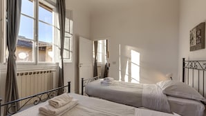 A bedroom with two beds, a radiator, and a window with curtains. - Greci 16 III in Firenze (Florence)