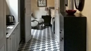 A narrow hallway with a checkered floor, leading to a bedroom with a bed, a nightstand, and a lamp. There is a mirror on the wall and a framed picture above the bed. - Mezzo 46 in Firenze With 2 Bedrooms and 2 Bathrooms (Florence)