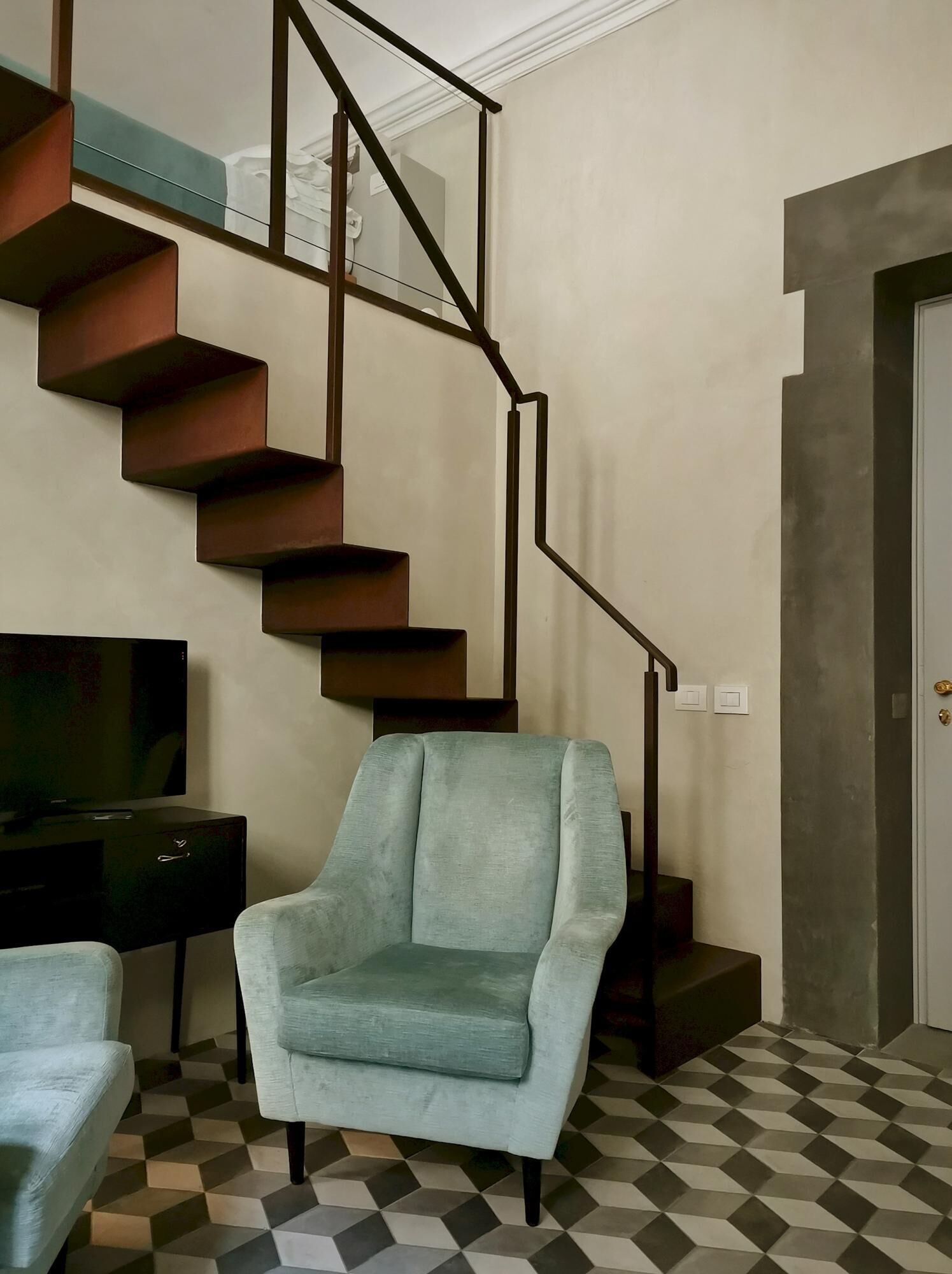 A living room with a checkered floor, a light blue armchair, a dark wooden TV stand, and a spiral staircase.