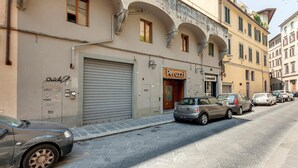 Une vue de rue avec des voitures garées, un magasin fermé dont l’enseigne indique « Peruzzi », et un bâtiment doté de fenêtres en arc de cercle.