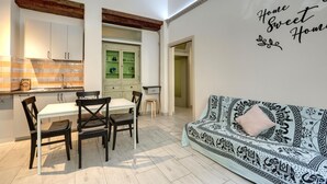 Un comedor con una mesa y sillas blancas, una cocina con armarios blancos y un sofá estampado con una sola almohada.