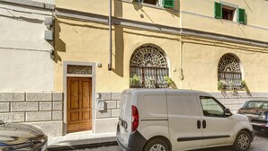 Una camioneta blanca estacionada frente a un edificio con puerta de madera y dos ventanas arqueadas con rejas de metal.
