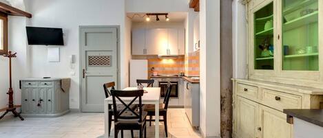 Cocina compacta con zona de comedor, televisor sobre la puerta y un armario con puertas de cristal.