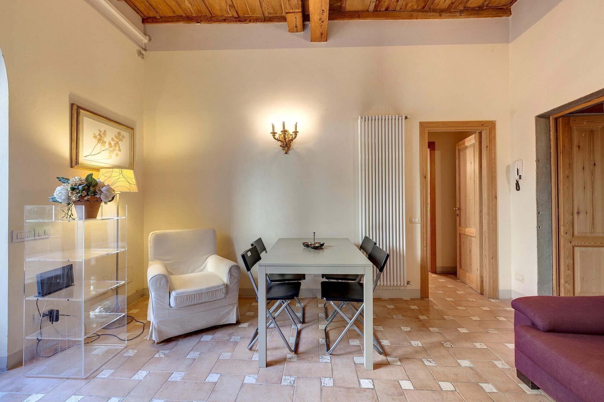 Uma área de refeições com mesa e cadeiras, uma poltrona branca, um sofá e um radiador.