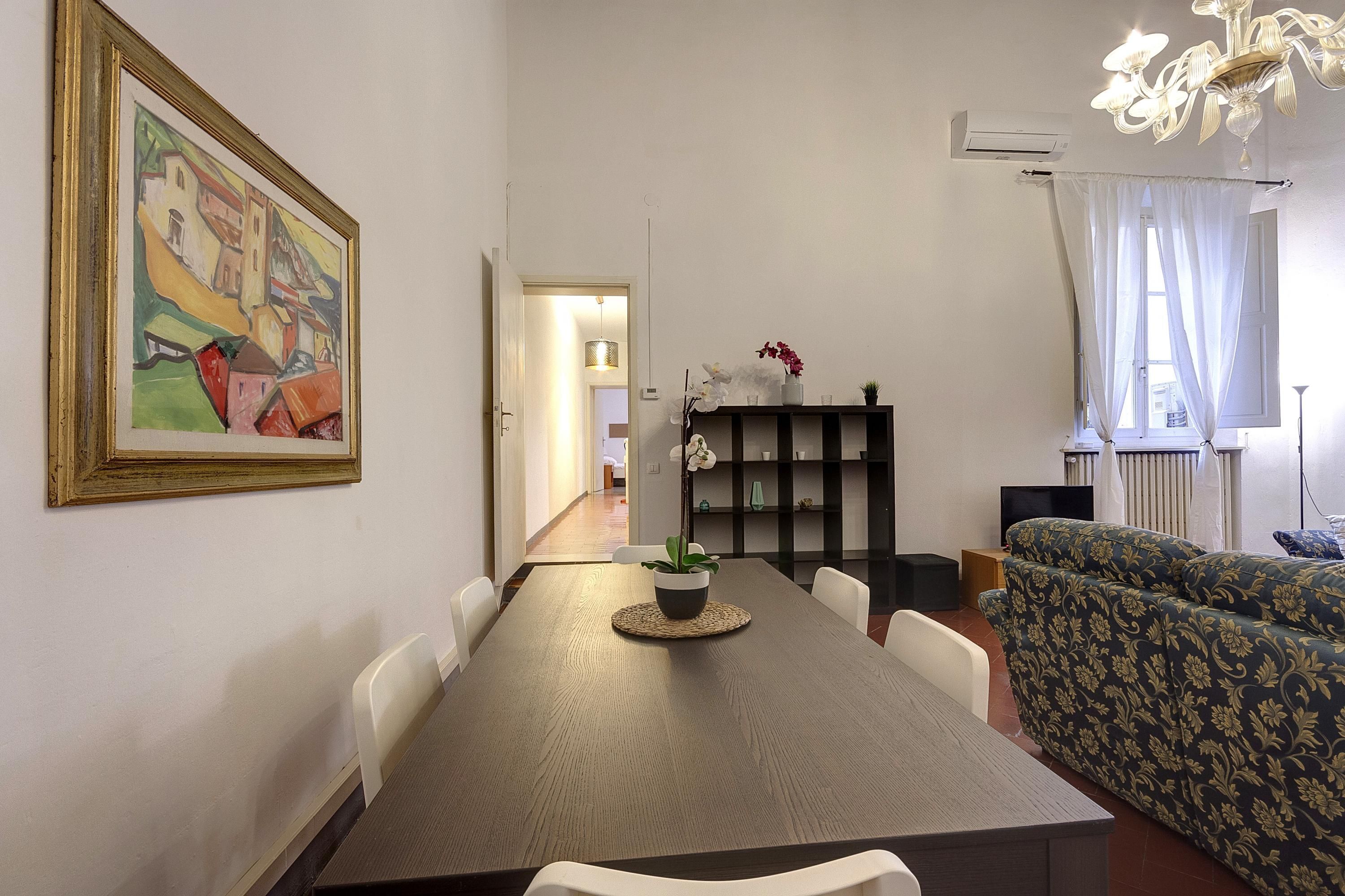 A dining area with a wooden table, chairs, a potted plant, and a sofa.