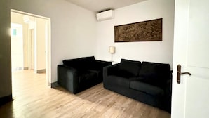 Uma sala de estar com dois sofás pretos, uma luminária branca e um quadro na parede.