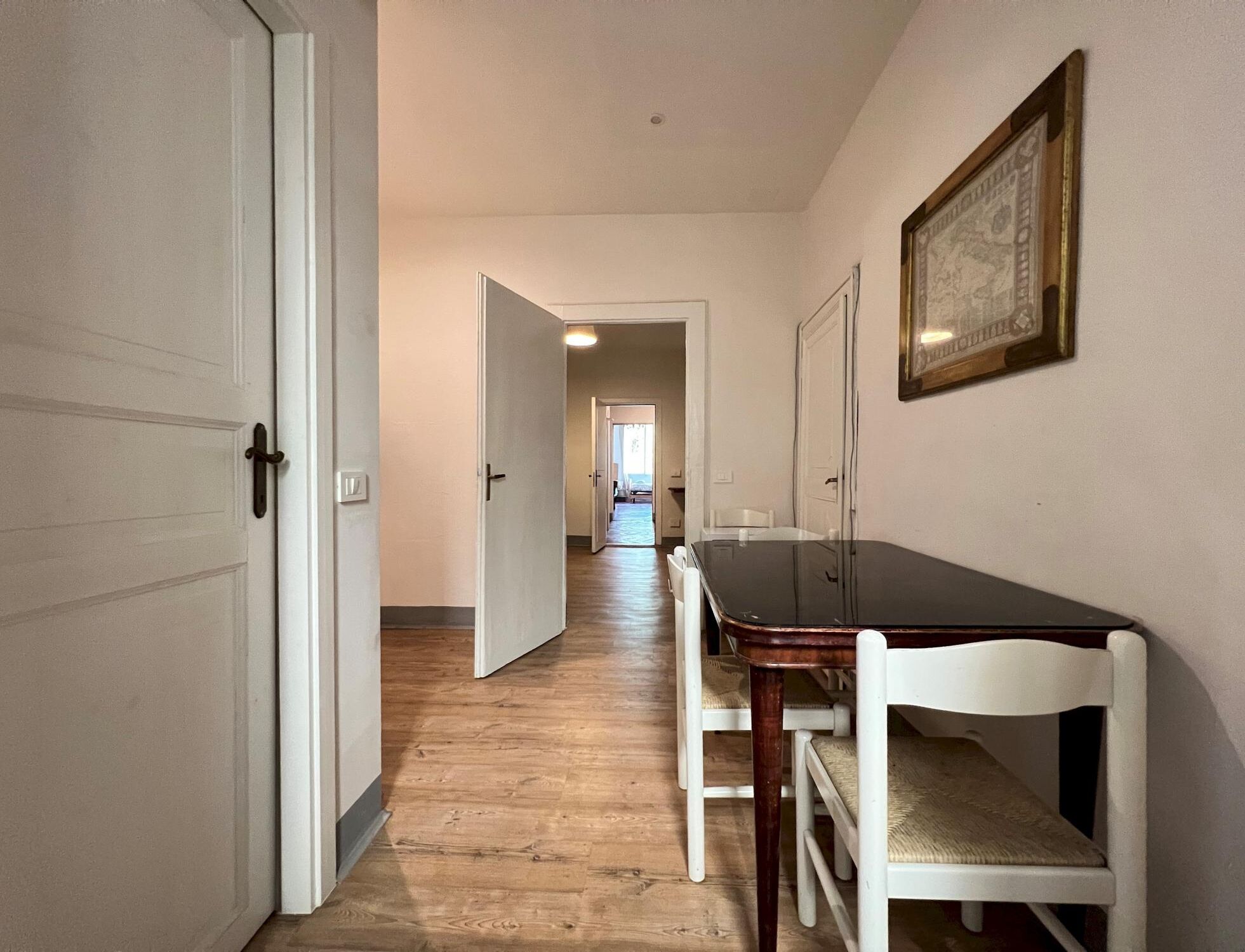 A hallway with a wooden floor, white doors, and a dining table with chairs.