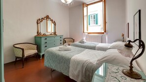 A bedroom with two beds, a dresser, a chair, a chandelier, and a window with shutters. - Pepi 51 in Firenze With 2 Bedrooms and 2 Bathrooms (Florence)