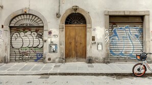 A building with two arched doors, one with graffiti and the other with a closed shutter. - Pepi 51 in Firenze With 2 Bedrooms and 2 Bathrooms (Florence)
