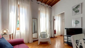 A spacious living room with a wooden floor, a red sofa, a white armchair, a TV, and a fireplace. - Santa Maria 10 in Firenze (Florence)