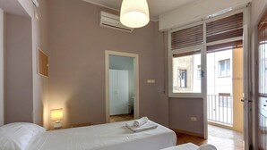A hotel room with two beds, a window with blinds, an air conditioning unit, and a door leading to a balcony. - Ponte Vecchio 4 Bedrooms (Florence)
