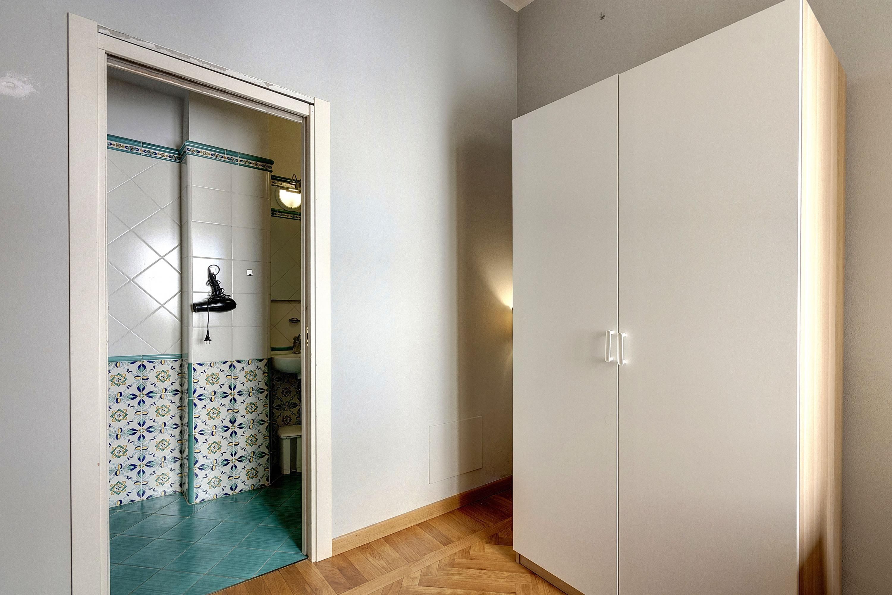 A hallway with a tiled wall, a wooden floor, and a white wardrobe.