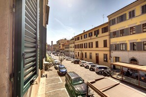 Vista da rua com carros estacionados, edifícios e um café com mesas ao ar livre.