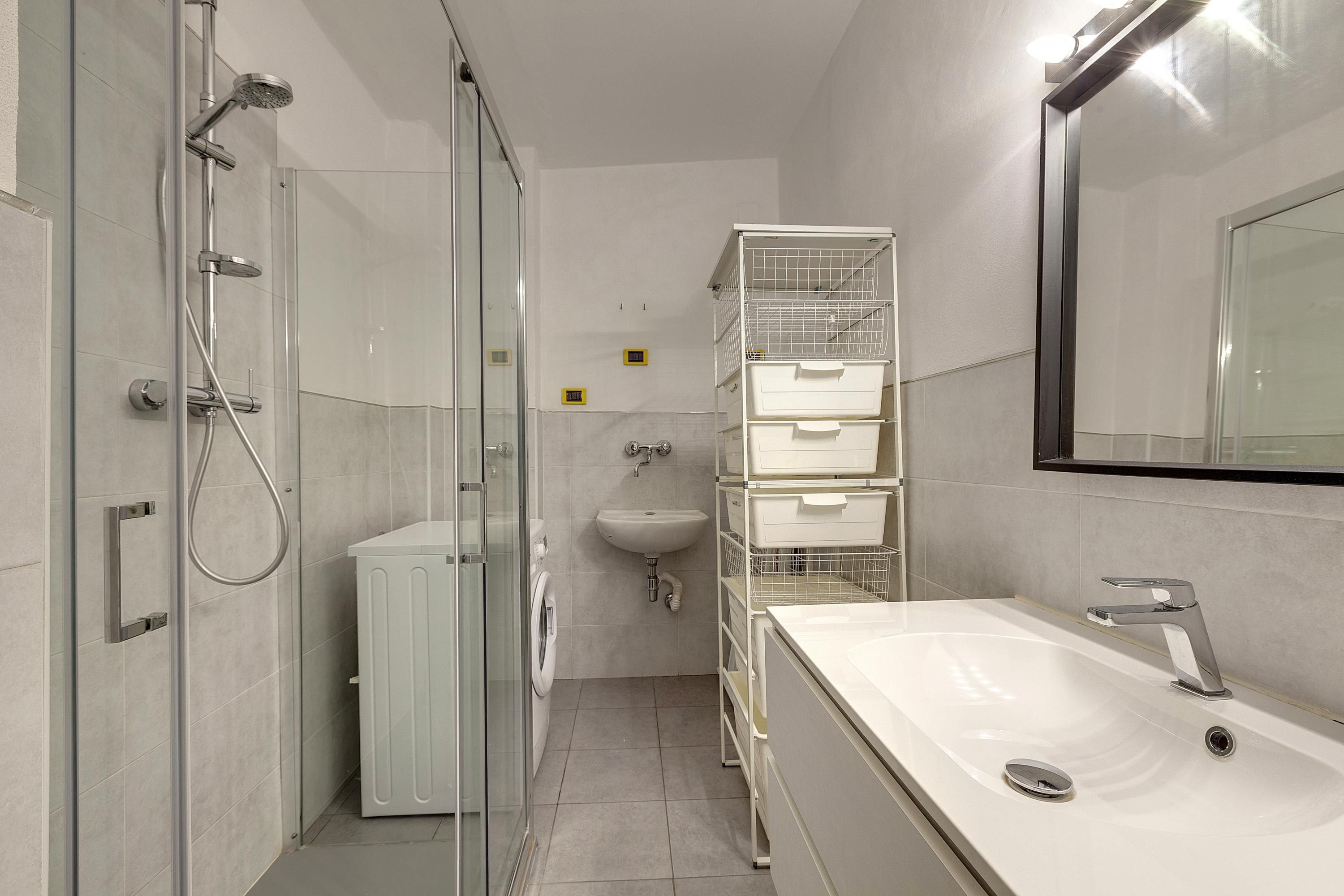 A modern bathroom with a glass shower enclosure, a white sink, and a mirror.