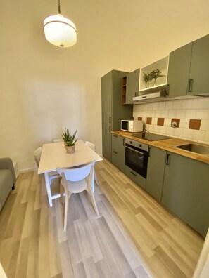 Una cocina compacta con una mesa blanca, armarios verdes, un microondas y un horno.