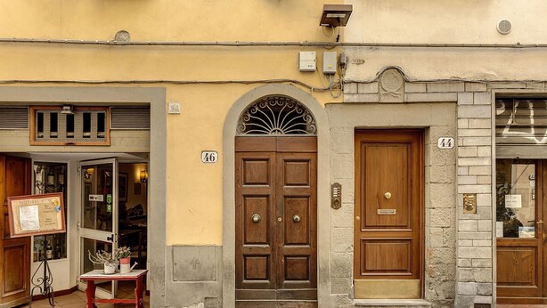 Ein Gebäude mit einer Holztür, die mit der Nummer 46 gekennzeichnet ist, einem Fenster mit grünen Rollläden und einem Schild vor der Fassade.