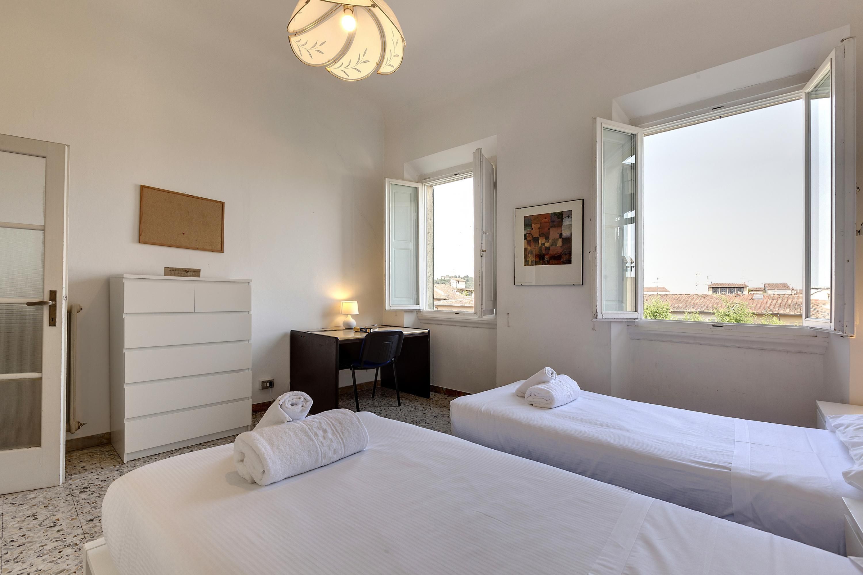 A hotel room with two beds, a desk, a chair, a dresser, and a window with a city view.