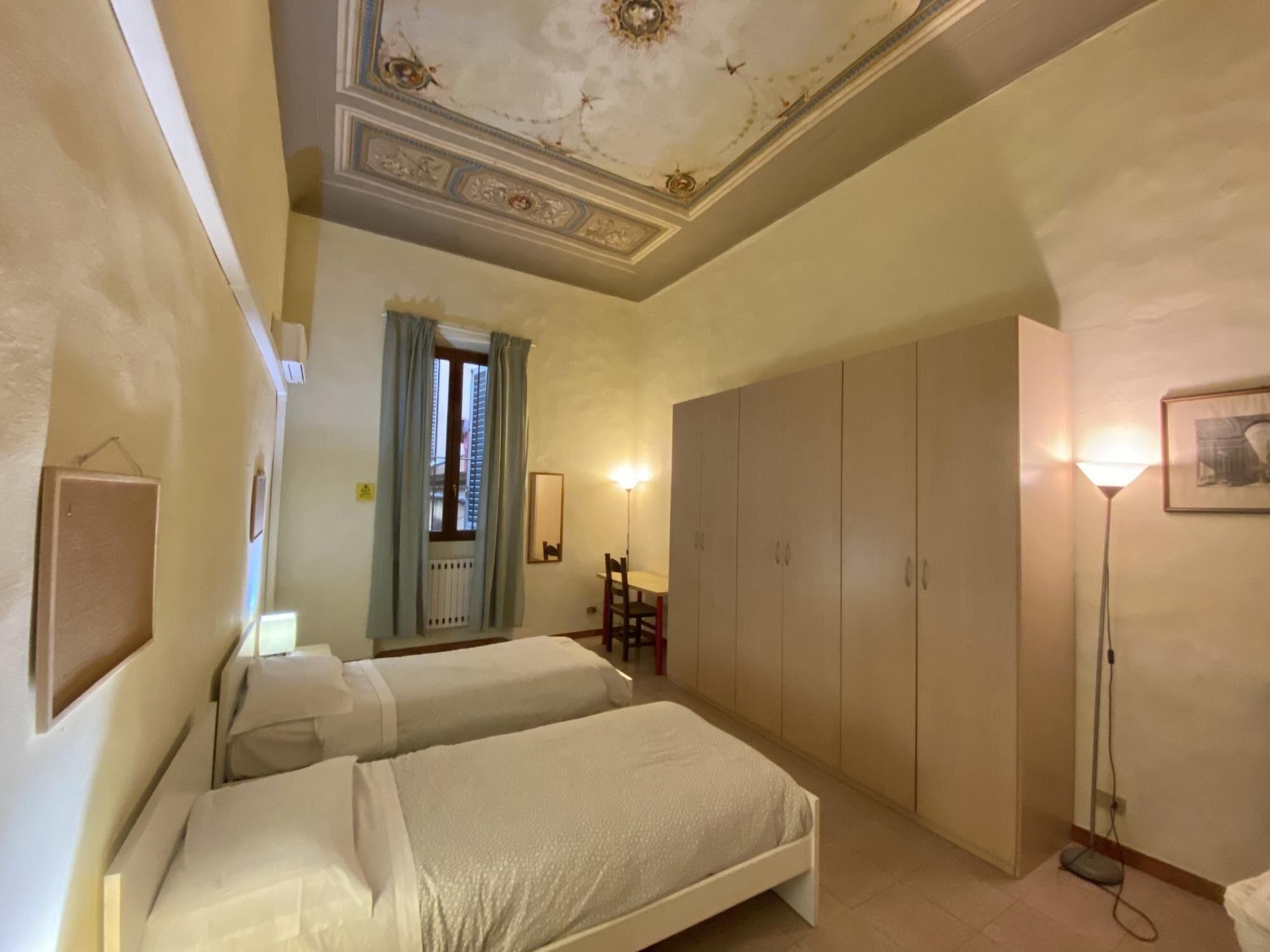 A bedroom with two beds, a wardrobe, a desk, and a chair.