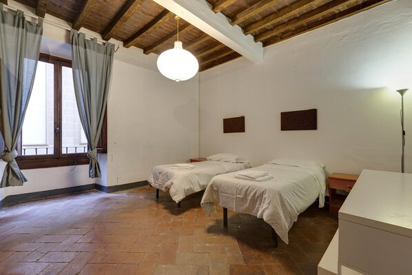 Une chambre avec deux lits, un plafond en bois, un bureau blanc et une fenêtre avec des rideaux.
