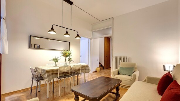 A modern living room with a wooden coffee table, a dining area with a table and chairs, and a sofa with red cushions. - Malenchini 6 in Firenze (Florence)