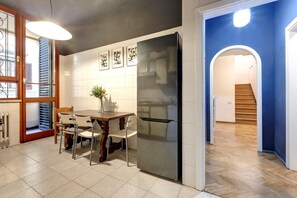Una cocina moderna con un refrigerador grande, una mesa de comedor con sillas y un florero con flores. Hay una escalera que conduce a otro nivel.