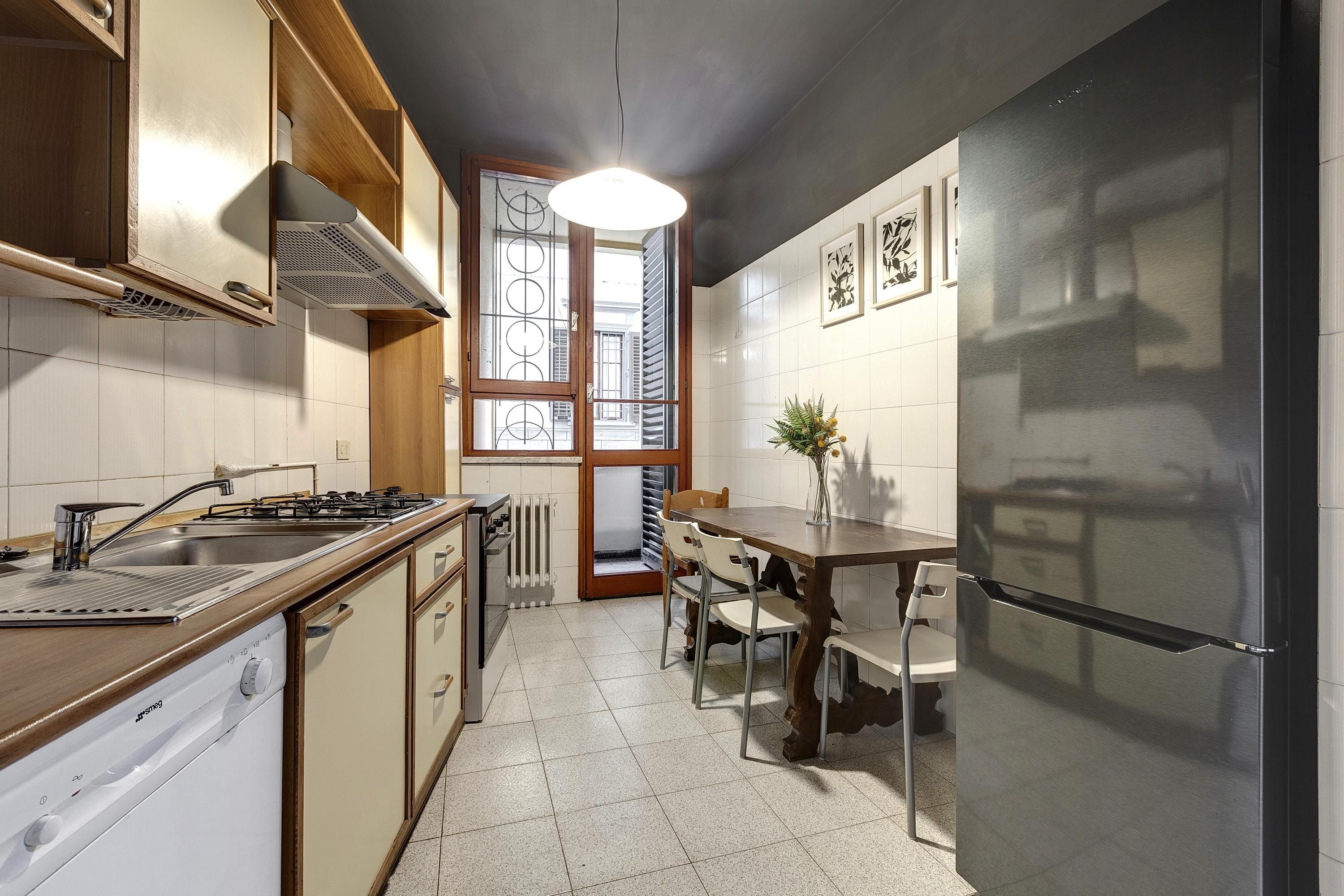 A modern kitchen with a built-in stove, sink, and refrigerator. There is a dining table with chairs and a window with a view of the outside.