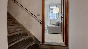 A staircase leading to a living room with a grey sofa and a hanging light fixture.