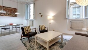 A modern living room with a white sofa, a coffee table, and a dining area with chairs and a table.