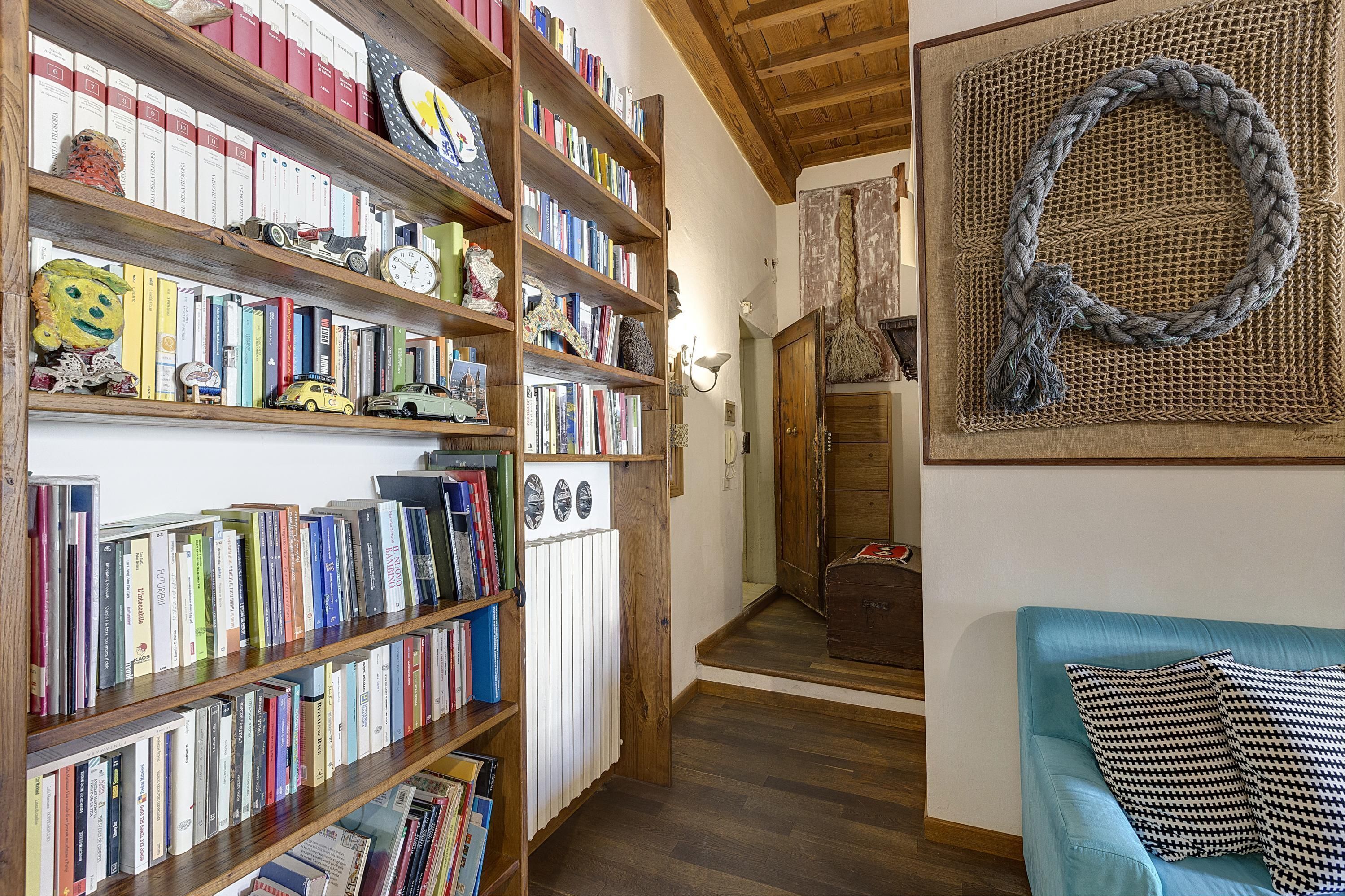 Una stanza con scaffali in legno pieni di libri, un divano blu e un decoro murale intrecciato.