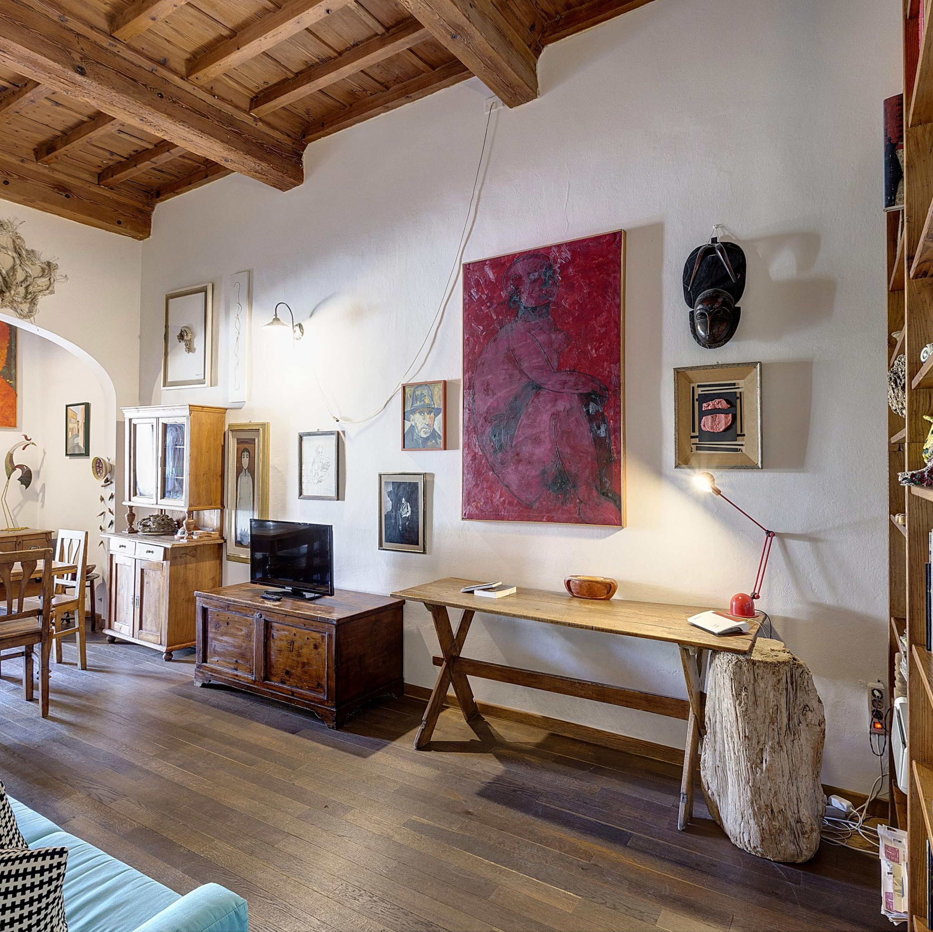 A cozy living room with wooden furniture, a large painting, and various framed artworks on the walls.