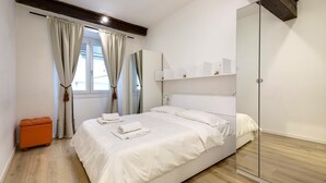 A bedroom with a bed, a wooden floor, a glass wardrobe, and a window with curtains.