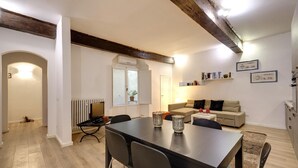 A modern living room with a dining area, featuring a wooden ceiling, white walls, and a sofa set.