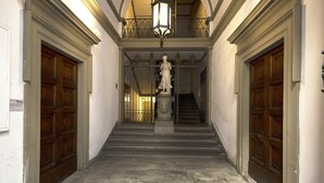 A hallway with two wooden doors, a statue, and a staircase leading to an upper level.
