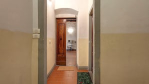 Un couloir étroit, avec une porte en bois au fond, un sol carrelé et un petit tapis orné d’un motif.