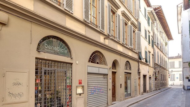 A street view with a building labeled "benedicta" featuring a closed shutter, a metal gate, and a sign indicating "servizio" and "fiaschetteria" services. - Benedetta 8 in Firenze (Florence)