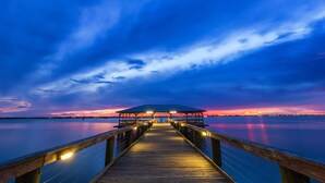 Un muelle de madera que conduce a una zona cubierta con vistas a un atardecer sobre el agua.