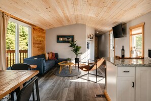 Interior acollidor d'una cabana amb sostre de fusta, un sofà blau, una taula de menjador i una cuina amb televisió.