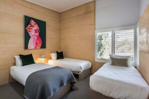 A room with two beds, a painting of a bird, and a window with blinds.