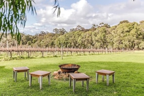 A grassy outdoor area with a fire pit and four wooden tables.