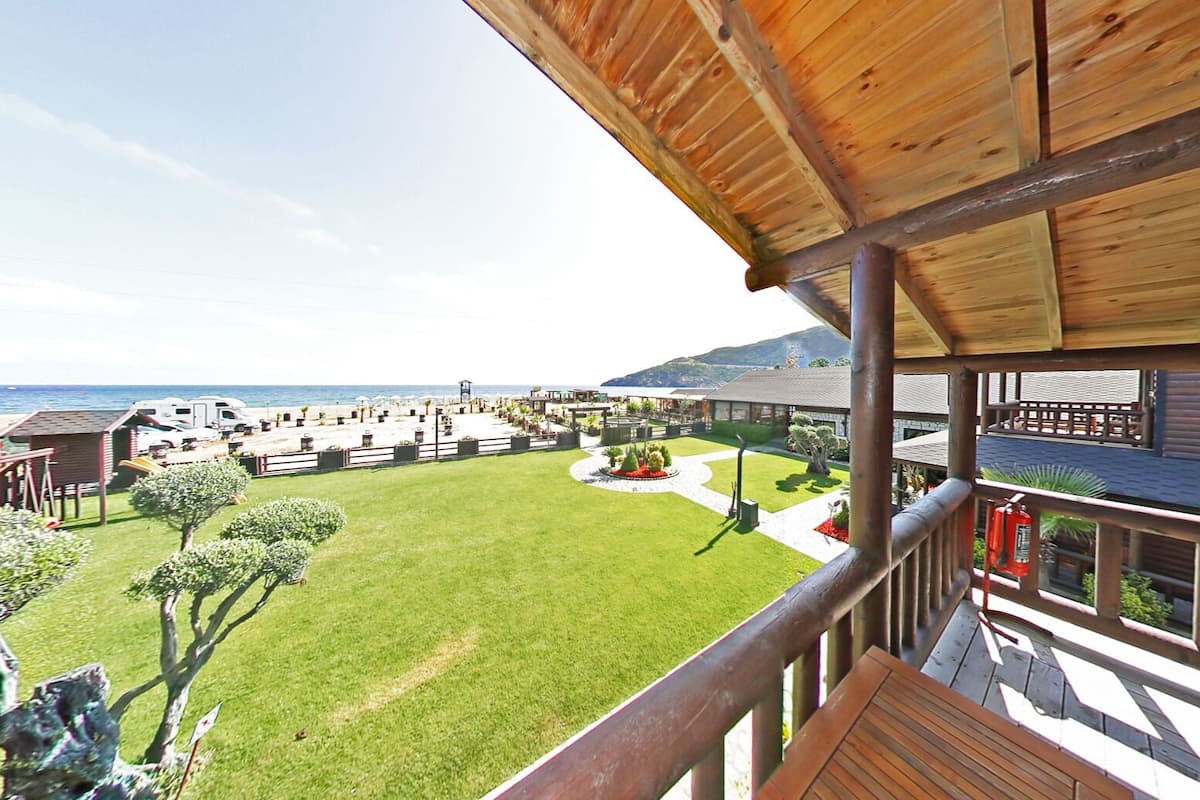 Blick vom Balkon auf eine gepflegte Rasenfläche mit Pool, Grillplatz und Meerblick.
