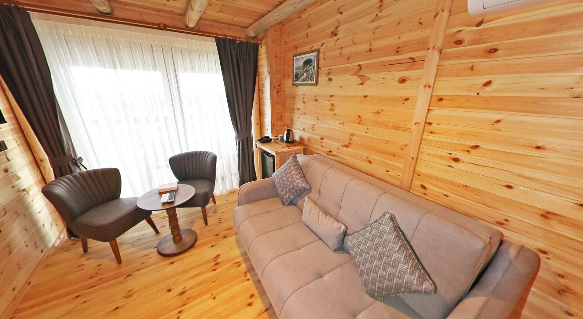 A wooden interior with a sofa, two armchairs, a small table, and a window with curtains.