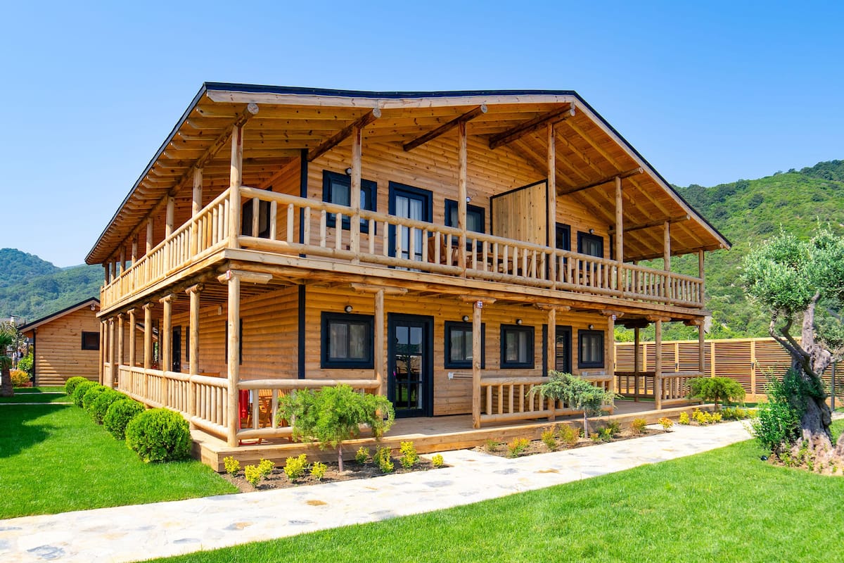 Eine zweistöckige Holzlodge mit Balkon, umgeben von gepflegten Rasenflächen vor einer Bergkulisse.