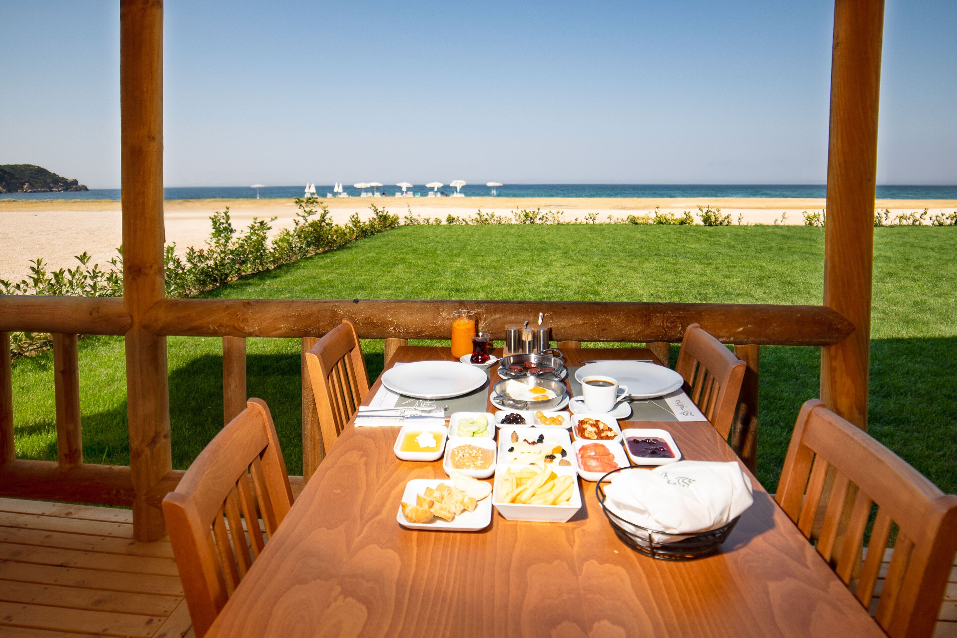 A wooden deck with a table set for breakfast overlooking a beach.