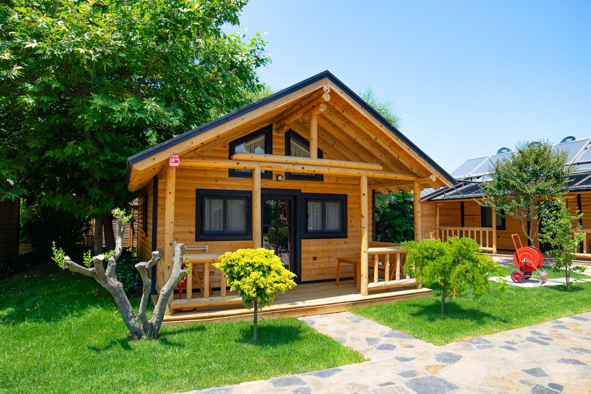 Eine Holzhütte mit Veranda, einem Kiesweg und einem kleinen Baum im Vorgarten.