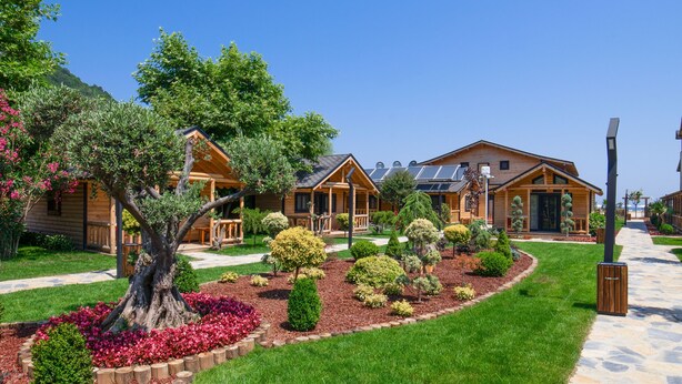 Une rangée de chalets en rondins, avec un jardin bien entretenu à l’avant, un sentier en pierre et un ciel bleu dégagé.