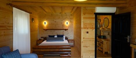 A wooden cabin interior with a bed, a sofa, a dining area, and a kitchen.