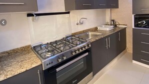 Una cuina moderna amb armaris foscos, una cuina de gas i un forn encastrat.
