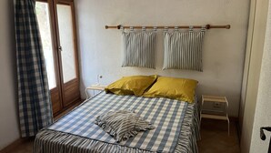 Ein Schlafzimmer mit karierter Bettdecke, zwei Kissen, einem Nachttisch und einem Fenster mit kariertem Vorhang.