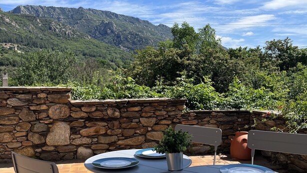 Eine Terrassensitzgelegenheit im Freien mit Steinmauern, einem Tisch und Stühlen sowie Blick auf die Berge.