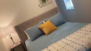 Un dormitorio con cama, mesita de noche, lámpara, ventana y un adorno en la pared.